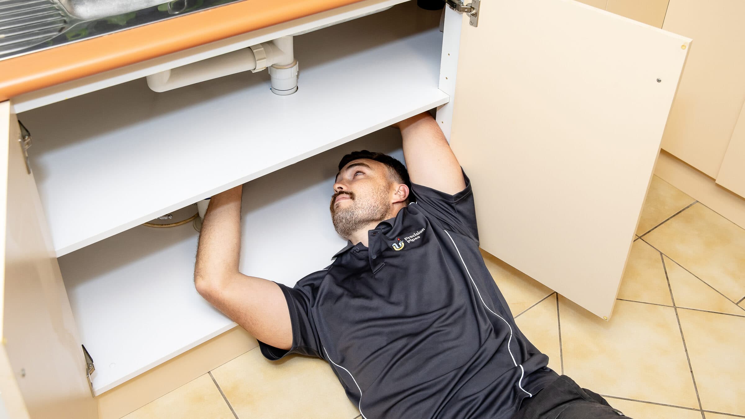 A Precision Pipes plumber lying beneath a kitchen sink checking the waste trap