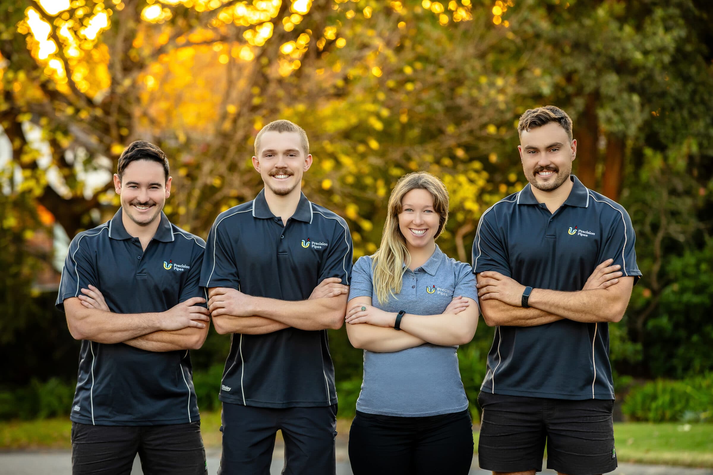 The four-person Precision Pipes team standing together in branded uniforms on a tree-lined street